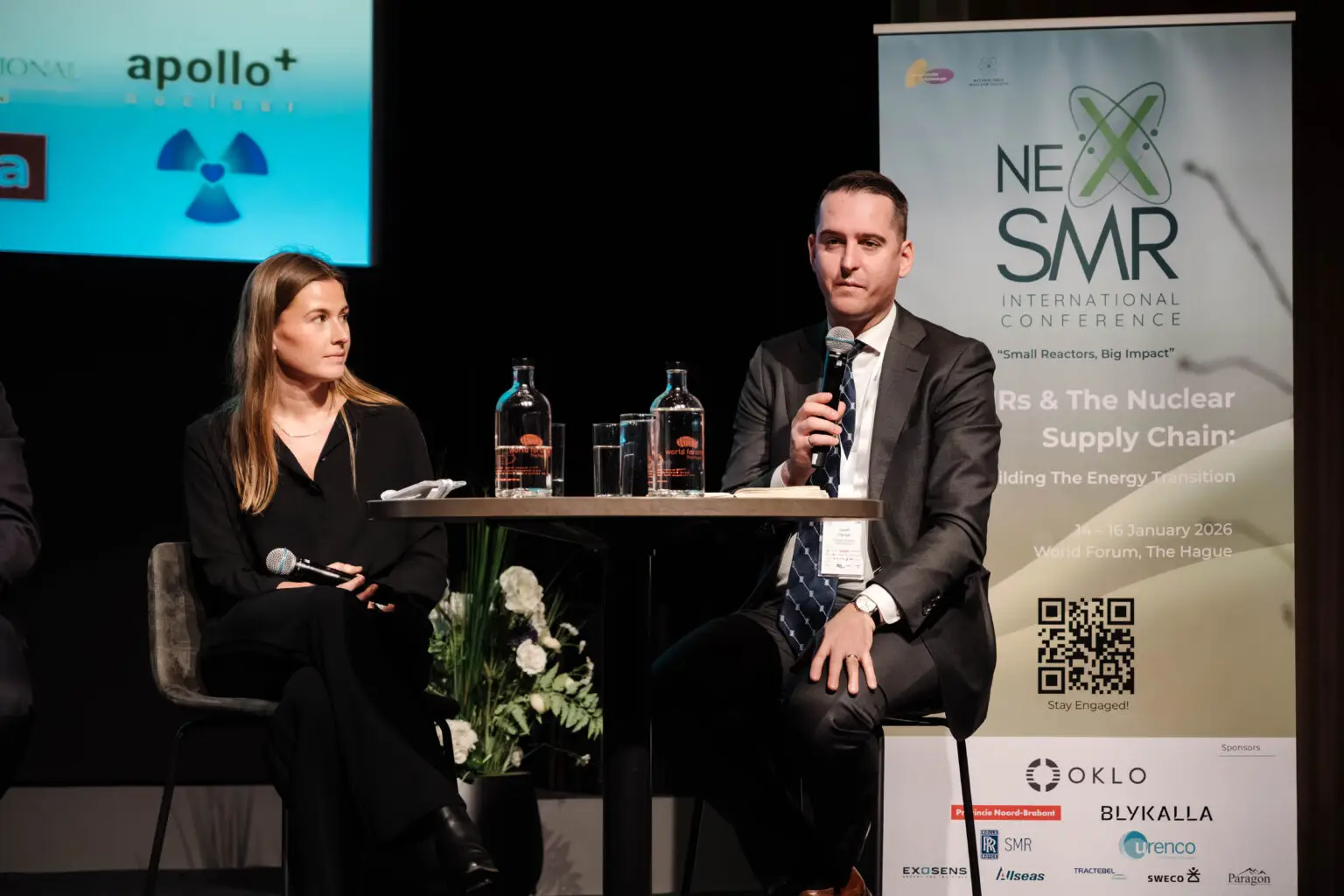 Seated expert discussion beside NexSMR conference branding